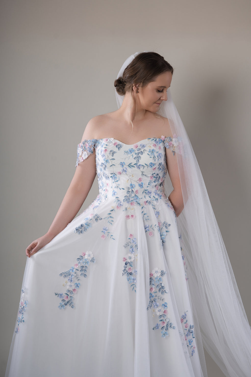 Romantic floral wedding gown featuring delicate blue, blush and ivory floral appliqués, paired with a dramatic cathedral-length veil.