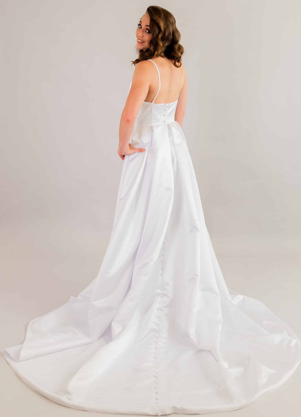 Back view of satin wedding gown featuring open back and decorative button details down the spine