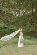 Bride in flowing ivory silk custom made dress with long sheer veil and greenery bouquet outdoors – Art Kollocsion Auckland