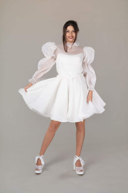 Model in white organza mini wedding dress with sheer ruffle collar, puff sleeves and full flared skirt, front view