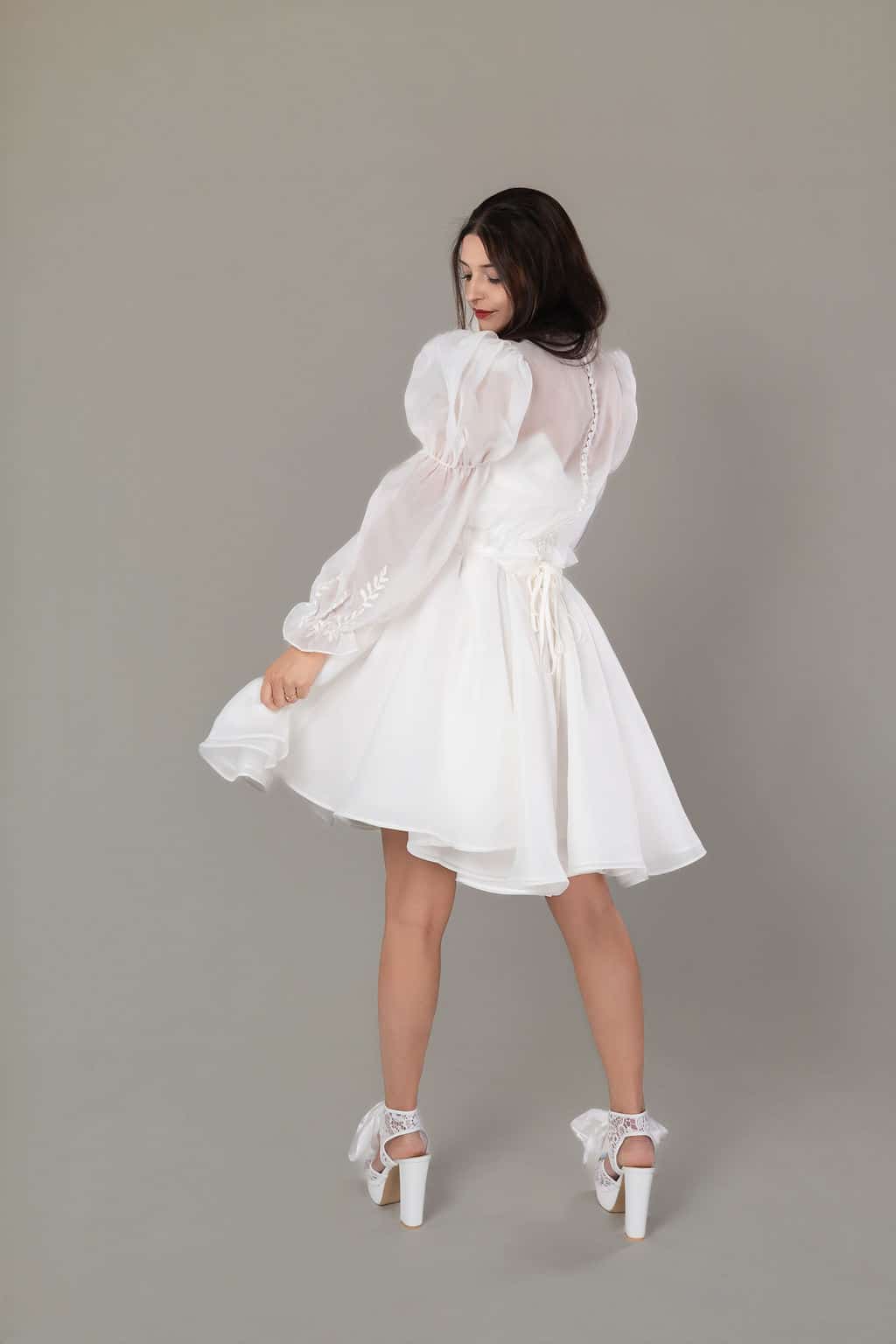 Back view of short white wedding dress showing sheer buttoned bodice, embroidered puff sleeves and corset ties