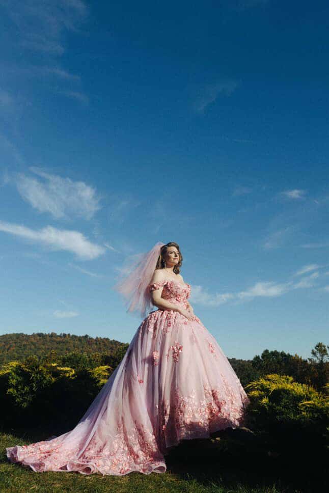 Full-length view of bride in pink tulle fairytale wedding gown with floral train against blue sky