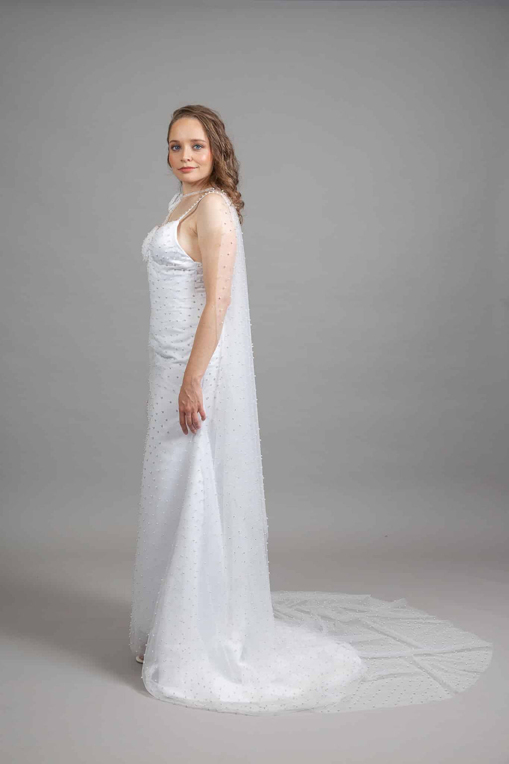 Model in side view of the fitted Beautiful Pearl Wedding Dress with scattered-pearl tulle cape and sweeping train