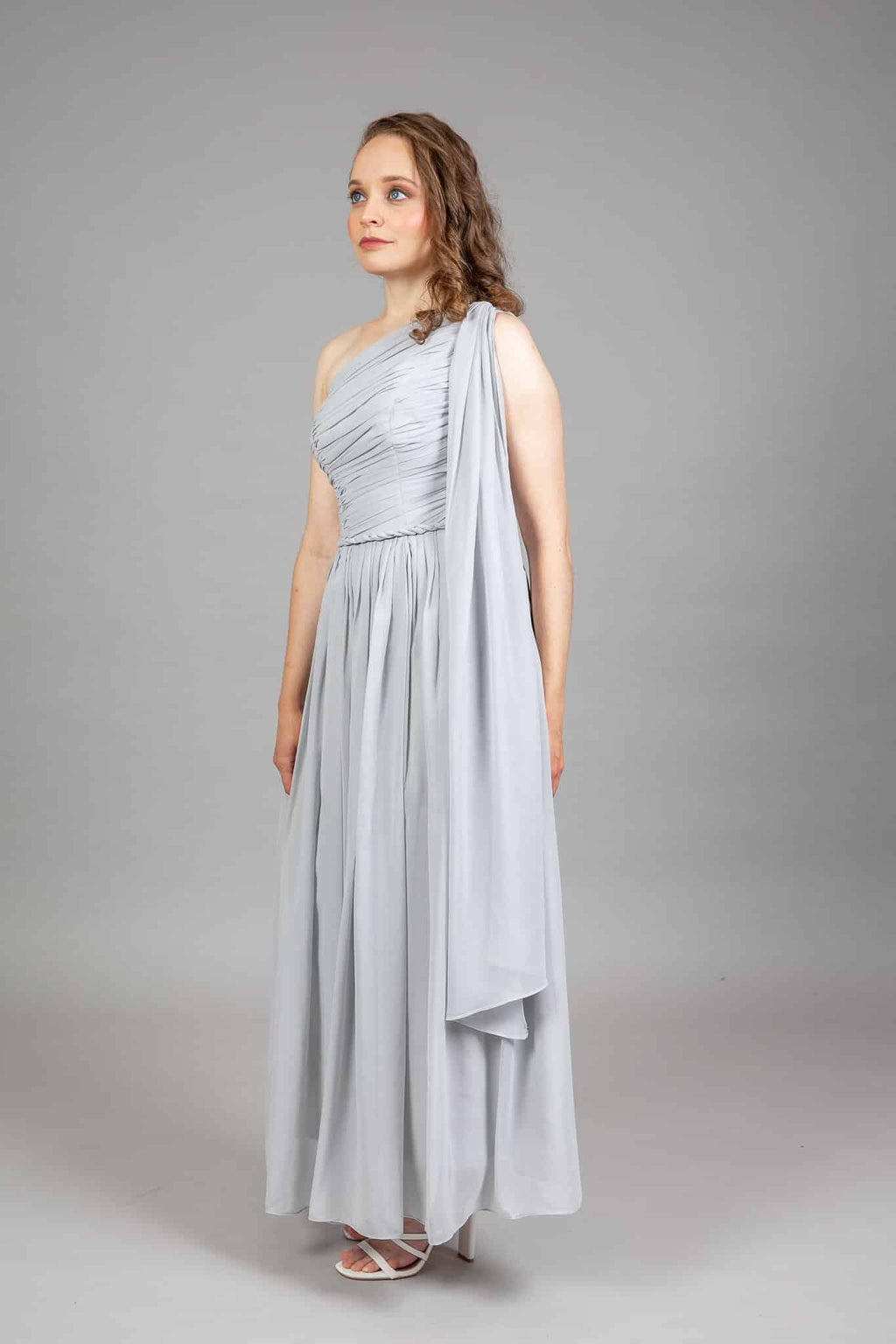 Side view of grey one-shoulder chiffon gown with ruched asymmetric bodice and long floating drape panel