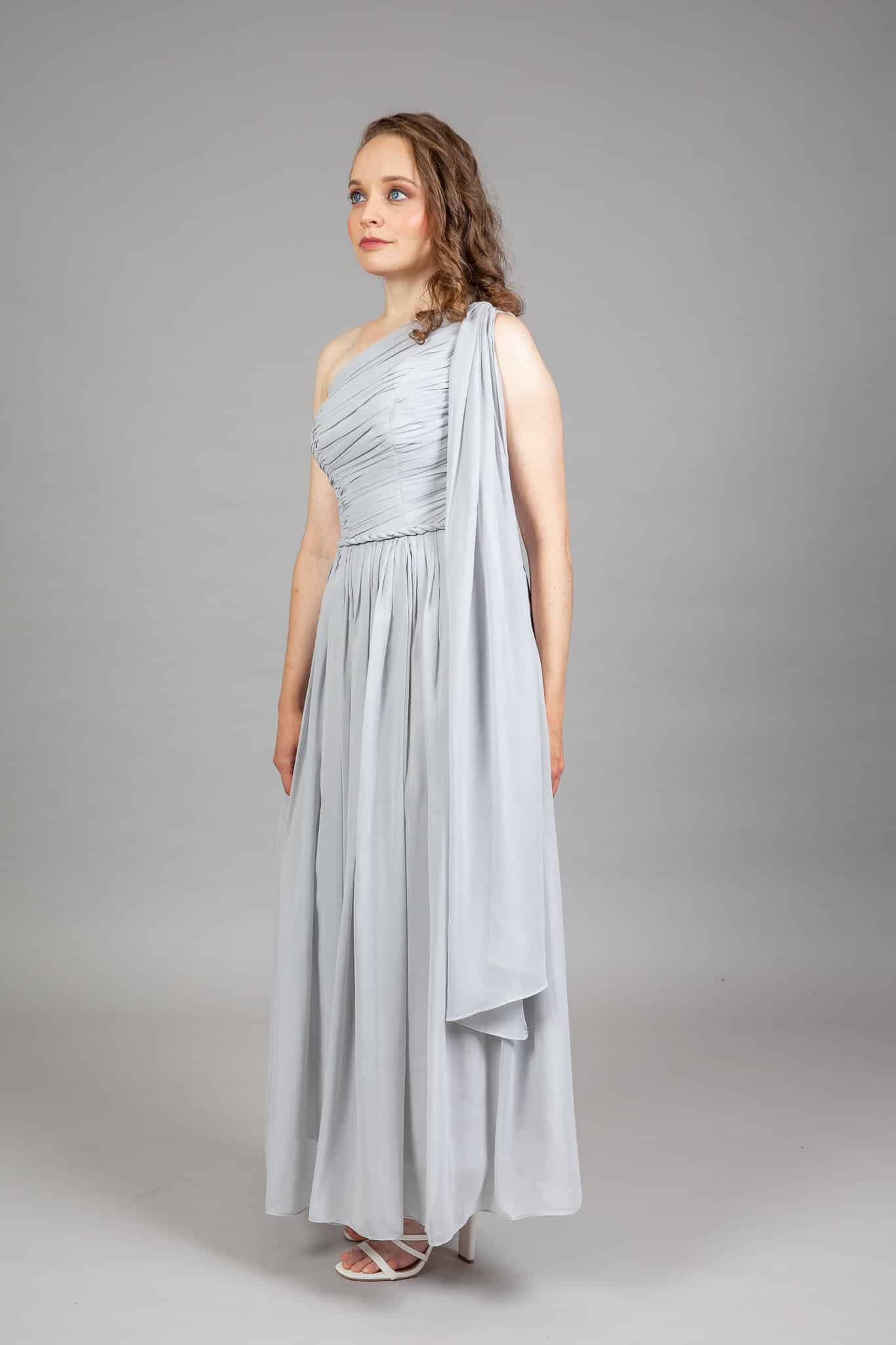 Side view of grey one-shoulder chiffon gown with ruched asymmetric bodice and long floating drape panel