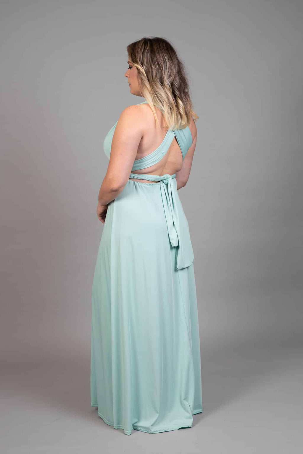 Side back view of mint green multiway dress with crossed back straps and long tie draping down the skirt