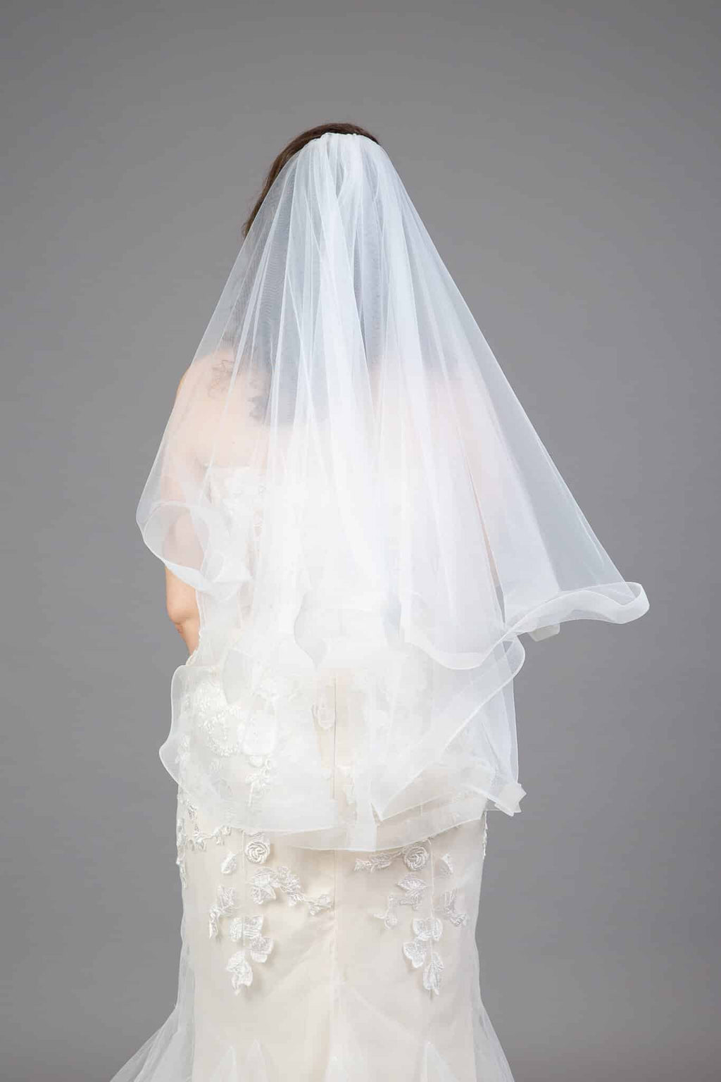 Back view of bride wearing horsehair edge veil with ruffled hem and flowing tulle layers
