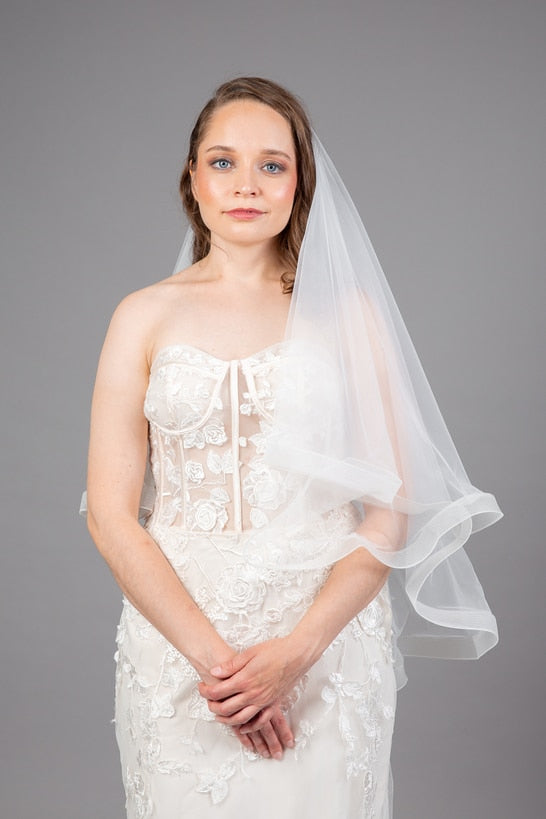 Close-up of sheer corset bodice with 3D floral lace appliqué, model holding a soft tulle veil