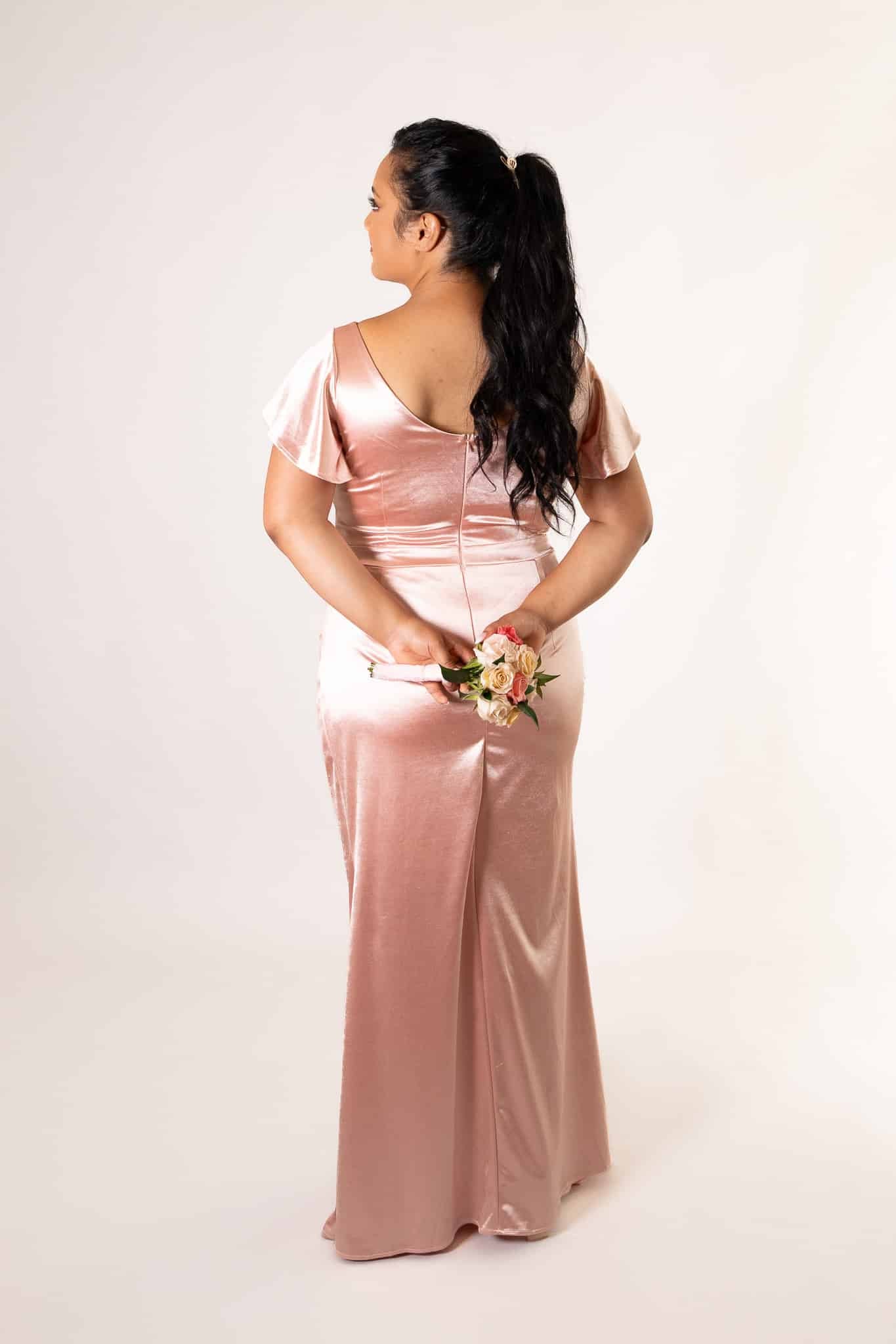 Back profile of blush satin dress highlighting V-neckline and elegant drape