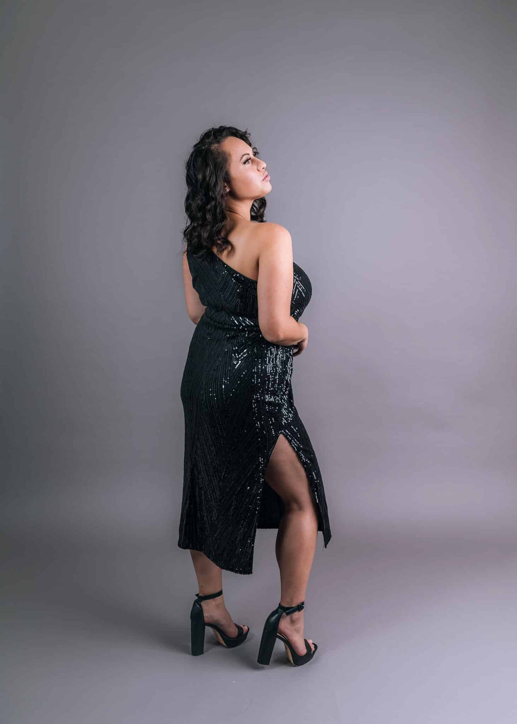 Black sequined dress with V-shaped patterned detail and thigh-high slit, back three-quarter view