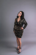 Model wearing black and gold sequin mini dress with wrap V-neckline, long sleeves and ruched skirt