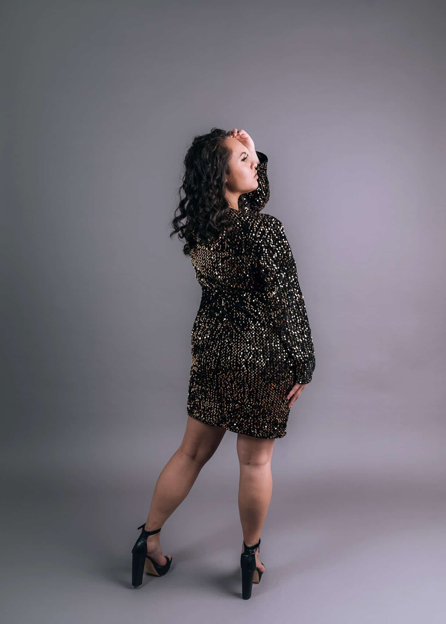Black long-sleeved dress with gold sequin embellishment, shown in profile against neutral backdrop