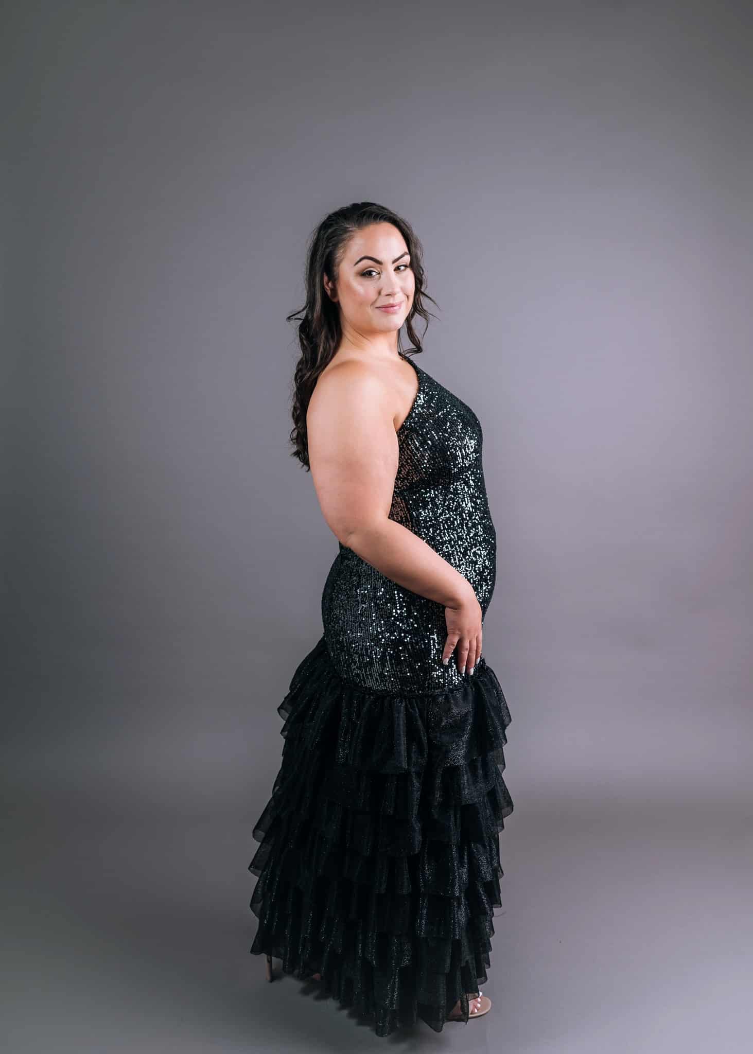 Three-quarter back view of black sequined gown with tiered tulle skirt and asymmetric design