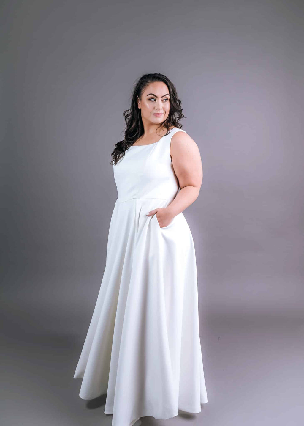 Side profile of white scoop neckline wedding gown with flowing skirt and functional pockets