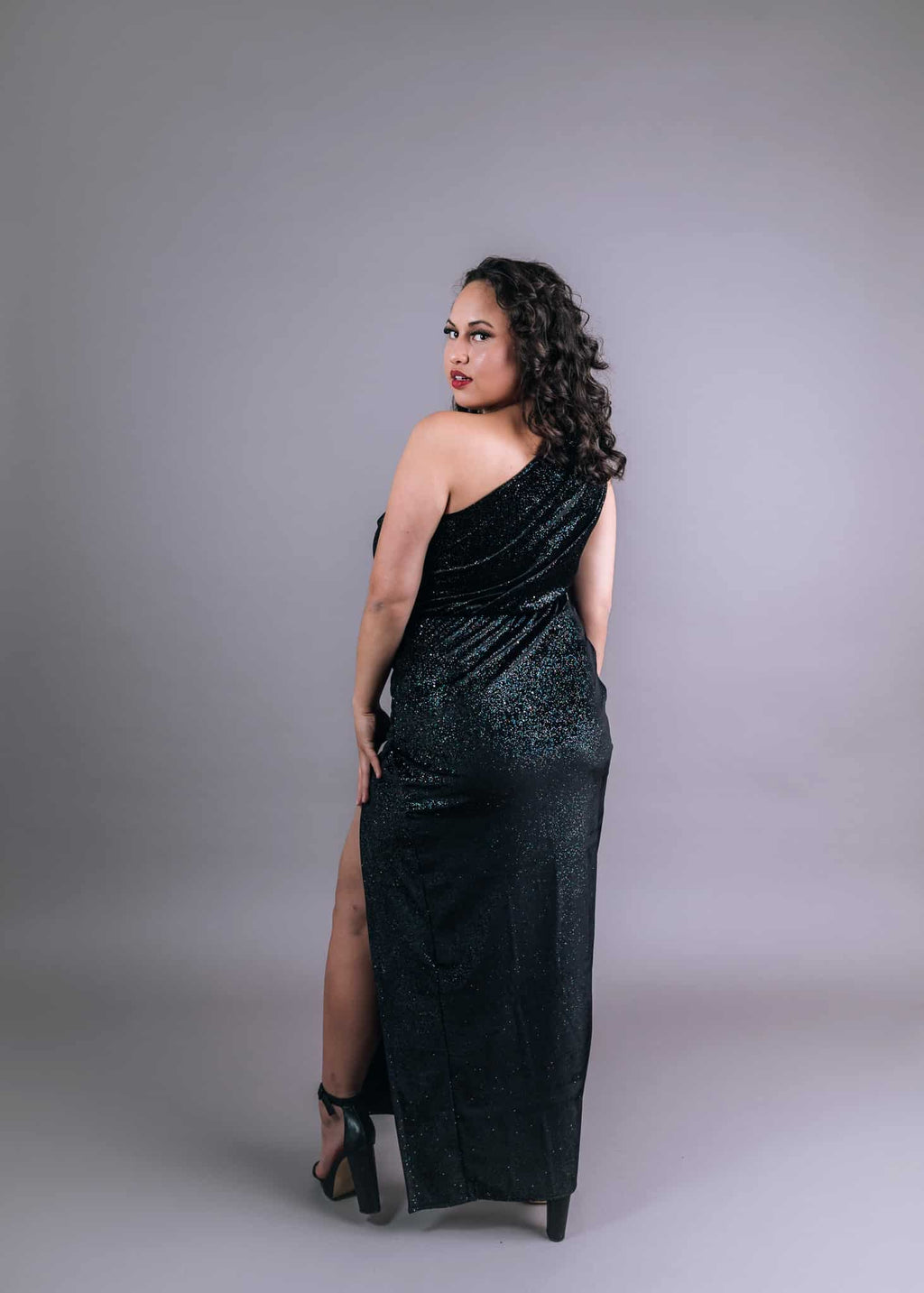 Model wearing black sequined one-shoulder gown with draped neckline and high slit, back view – Art Kollocsion Auckland