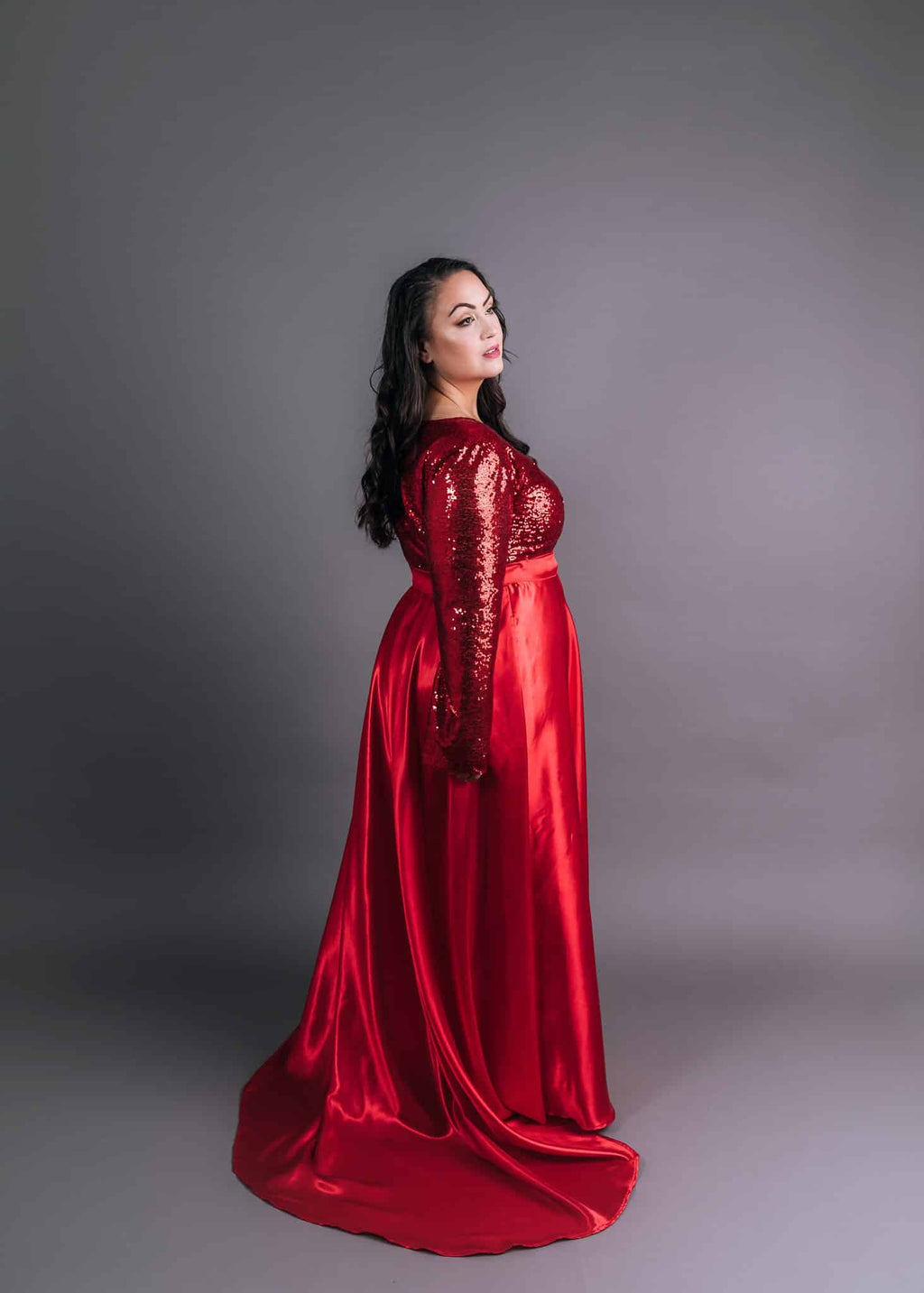 Red sequin gown with long sleeves and flowing satin skirt, side profile view