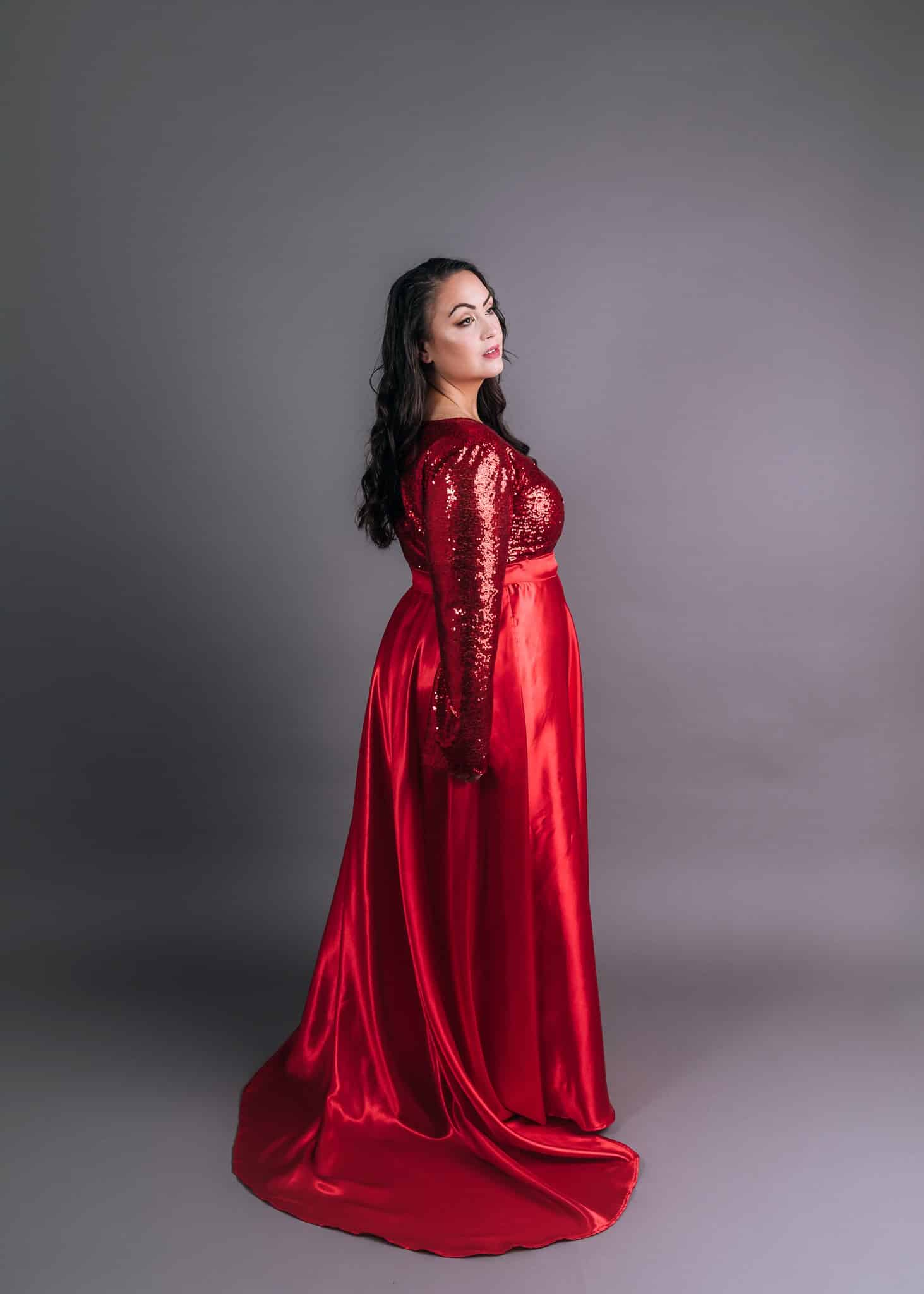 Red sequin gown with long sleeves and flowing satin skirt, side profile view