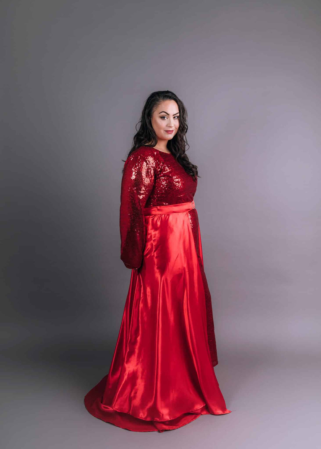 Red formal gown featuring sequined long sleeves, cinched waist, and full satin train