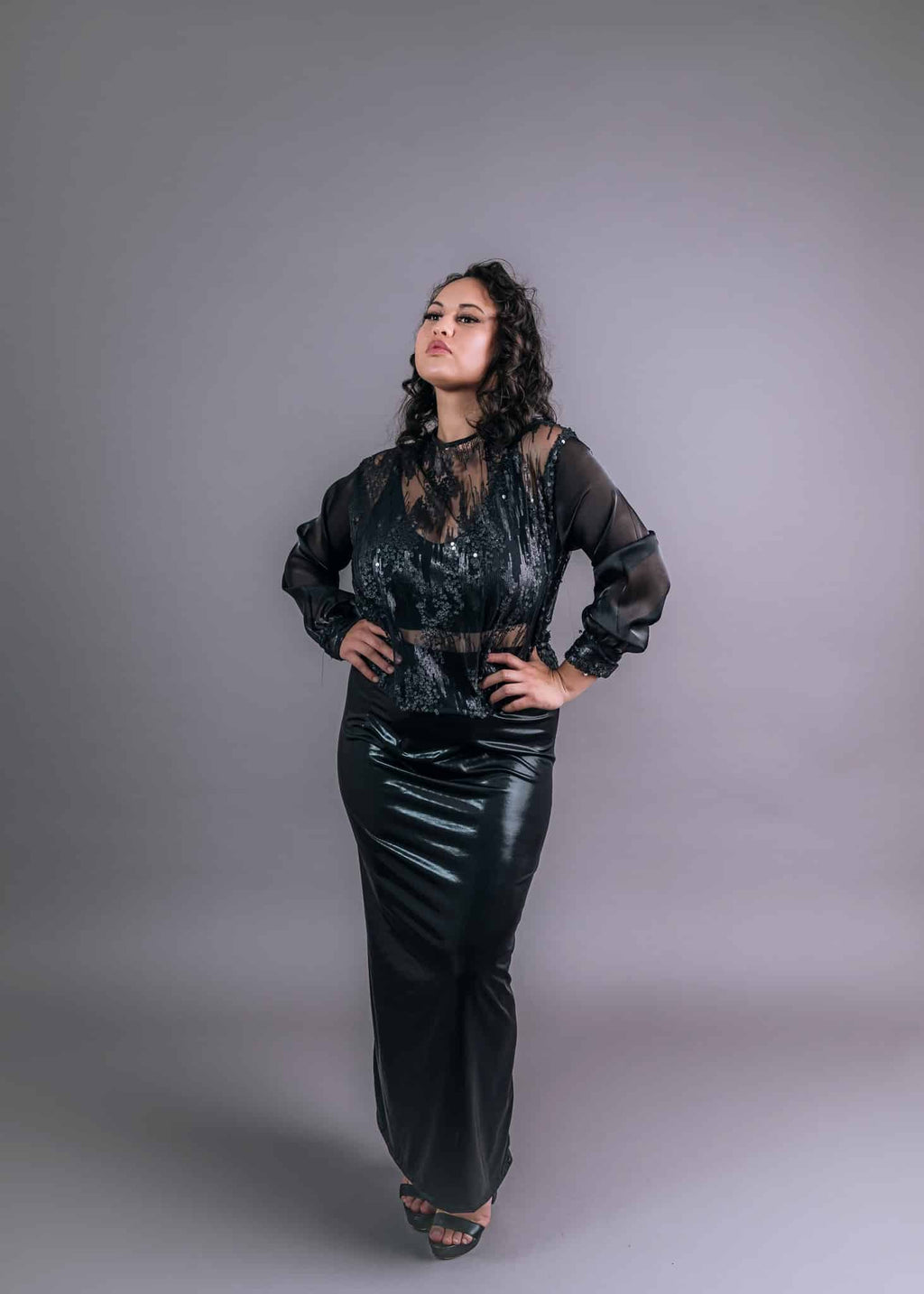 Model wearing black sequin bodice with sheer balloon sleeves and glossy satin midi skirt, front view