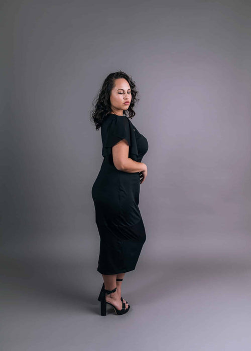 Side view of model wearing a black flutter attachable sleeve draped over the shoulder of a fitted midi dress