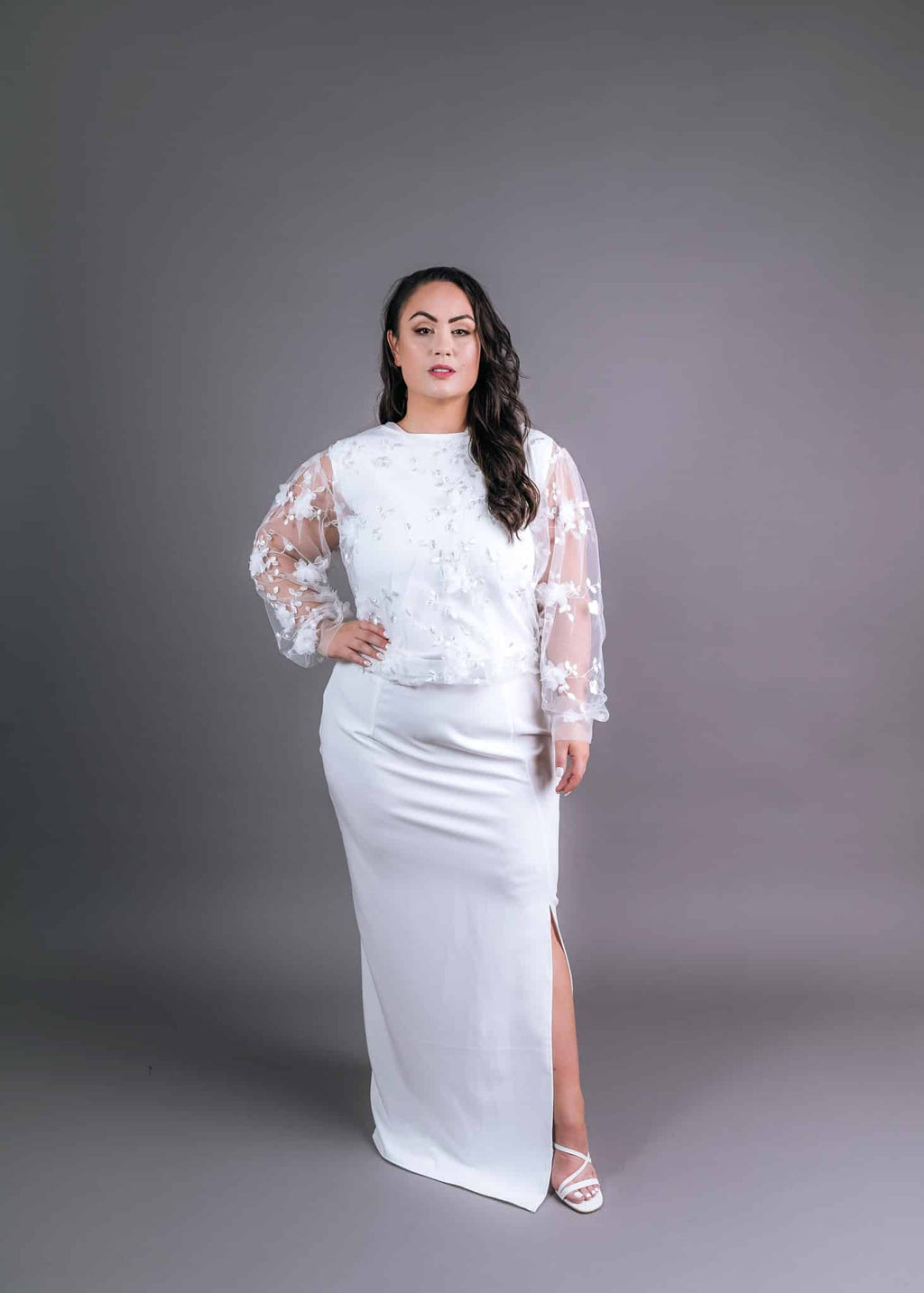Ivory reception outfit with embellished bodice and sheer floral lace sleeves, paired with fitted maxi skirt and side slit