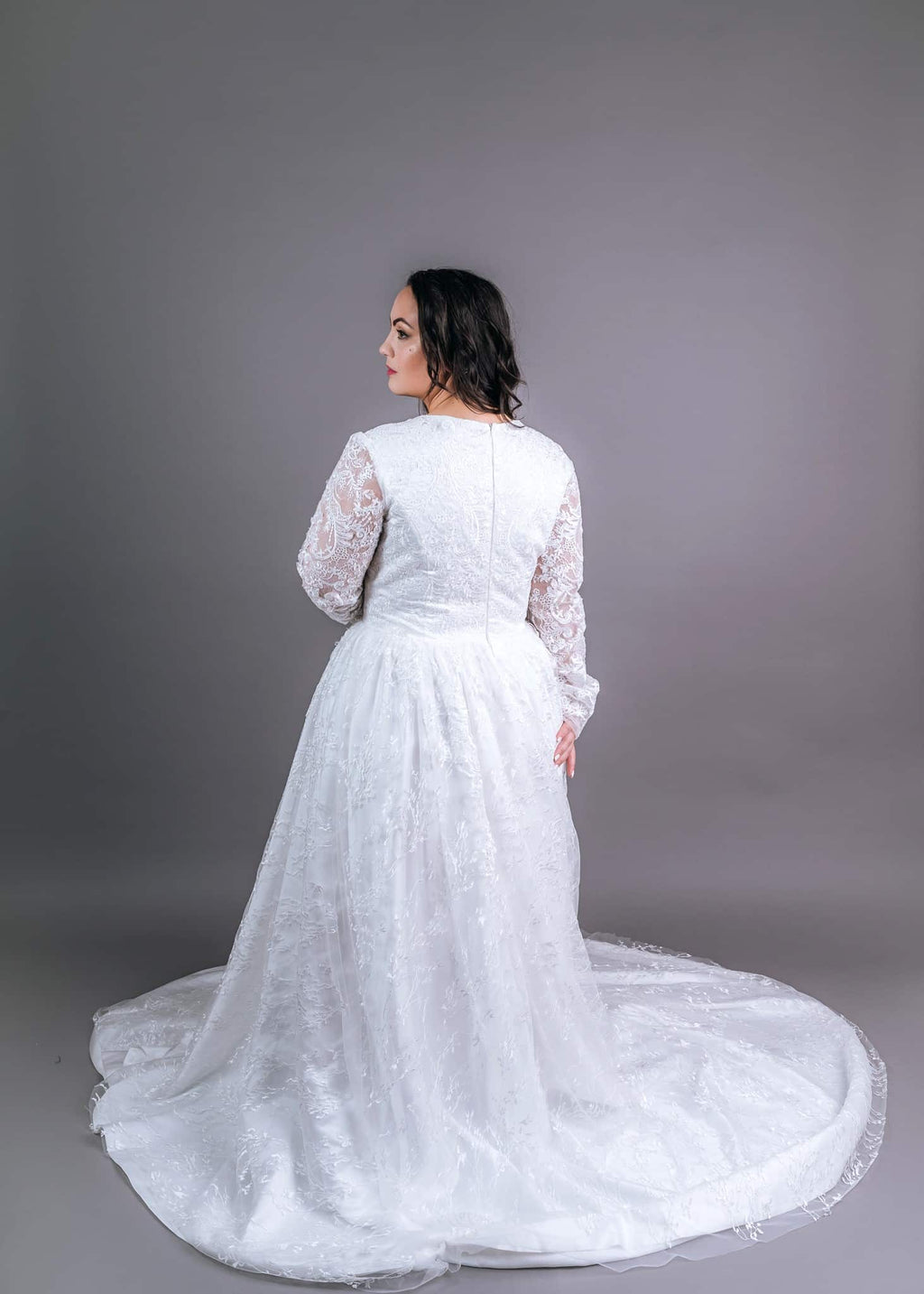 Back view of white lace A-line wedding gown with long sheer sleeves and sweeping train spread across the floor
