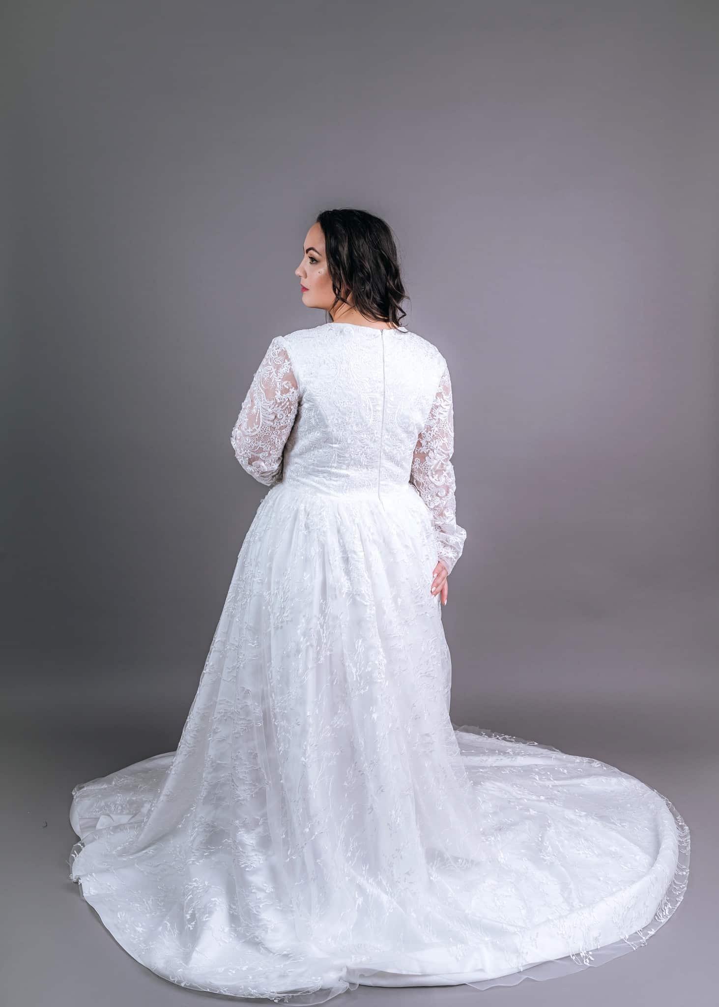 Back view of white lace A-line wedding gown with long sheer sleeves and sweeping train spread across the floor