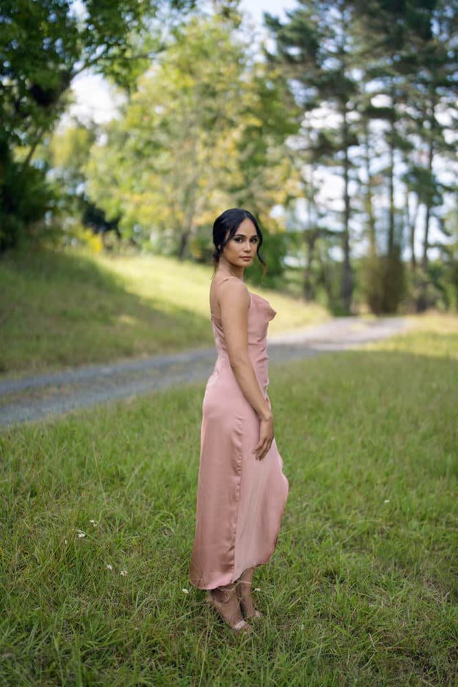 Model in rose pink bias-cut satin slip dress, side angle showing the flowing skirt and draped cowl front