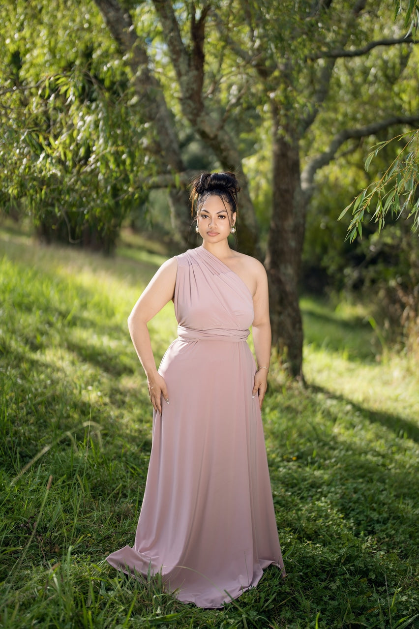 Dusty pink multiway infinity dress styled one-shoulder, full-length front view on model in a garden