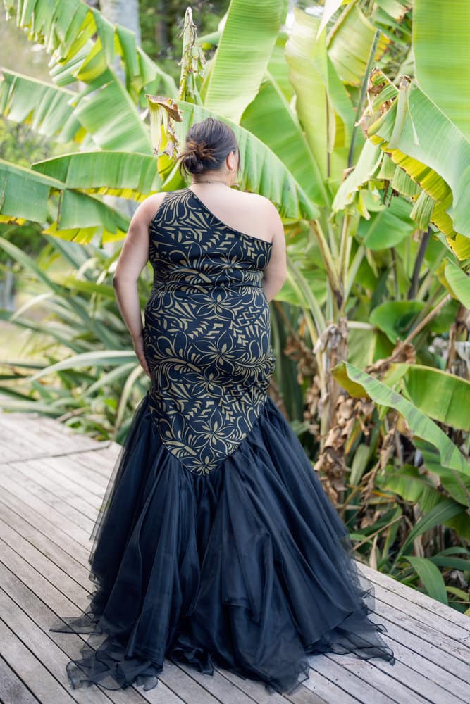 Back view of navy ball gown showing detailed gold embroidered Polynesian motifs and cascading tulle train