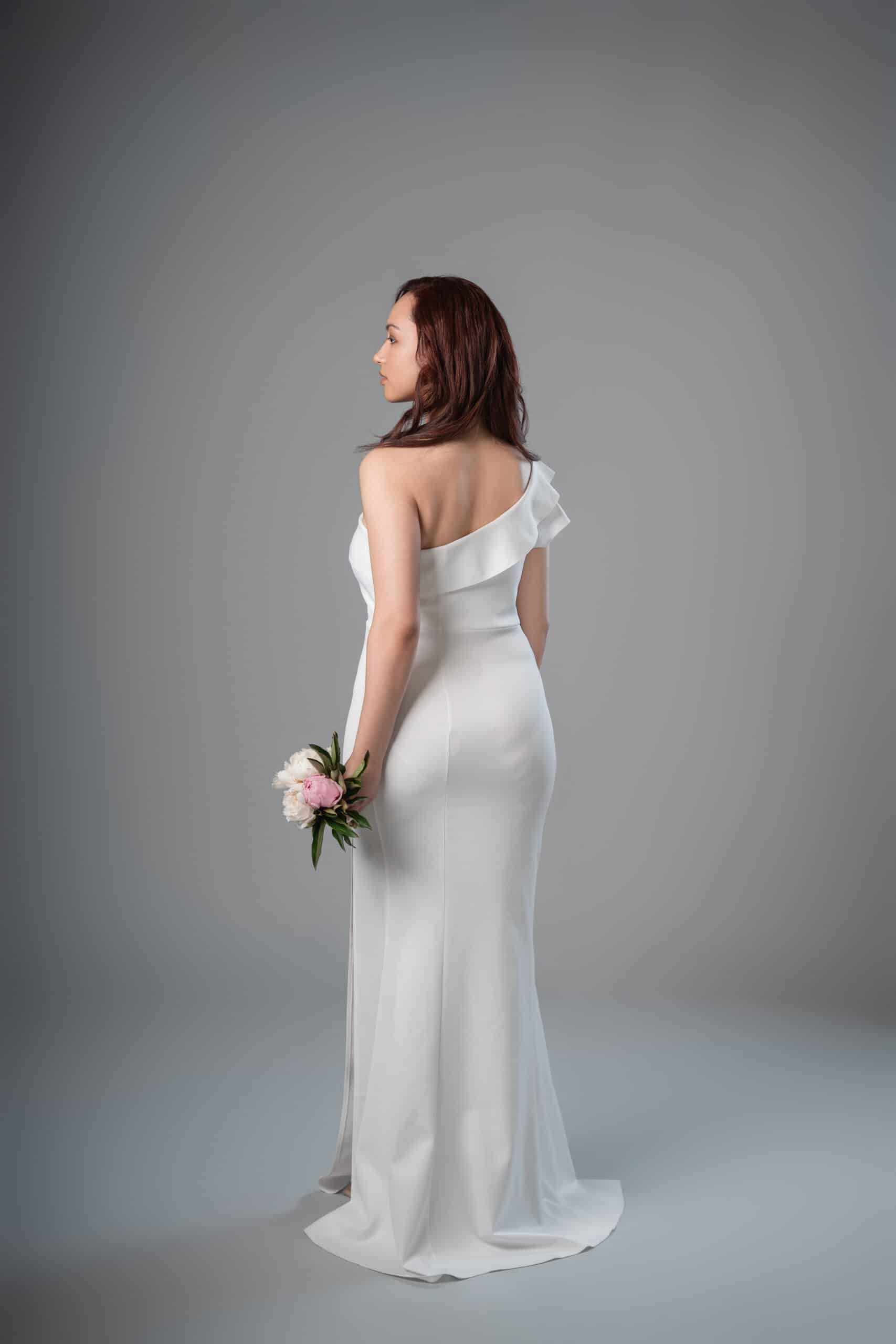 Back view of white one-shoulder dress with asymmetrical ruffle detail and flowing train