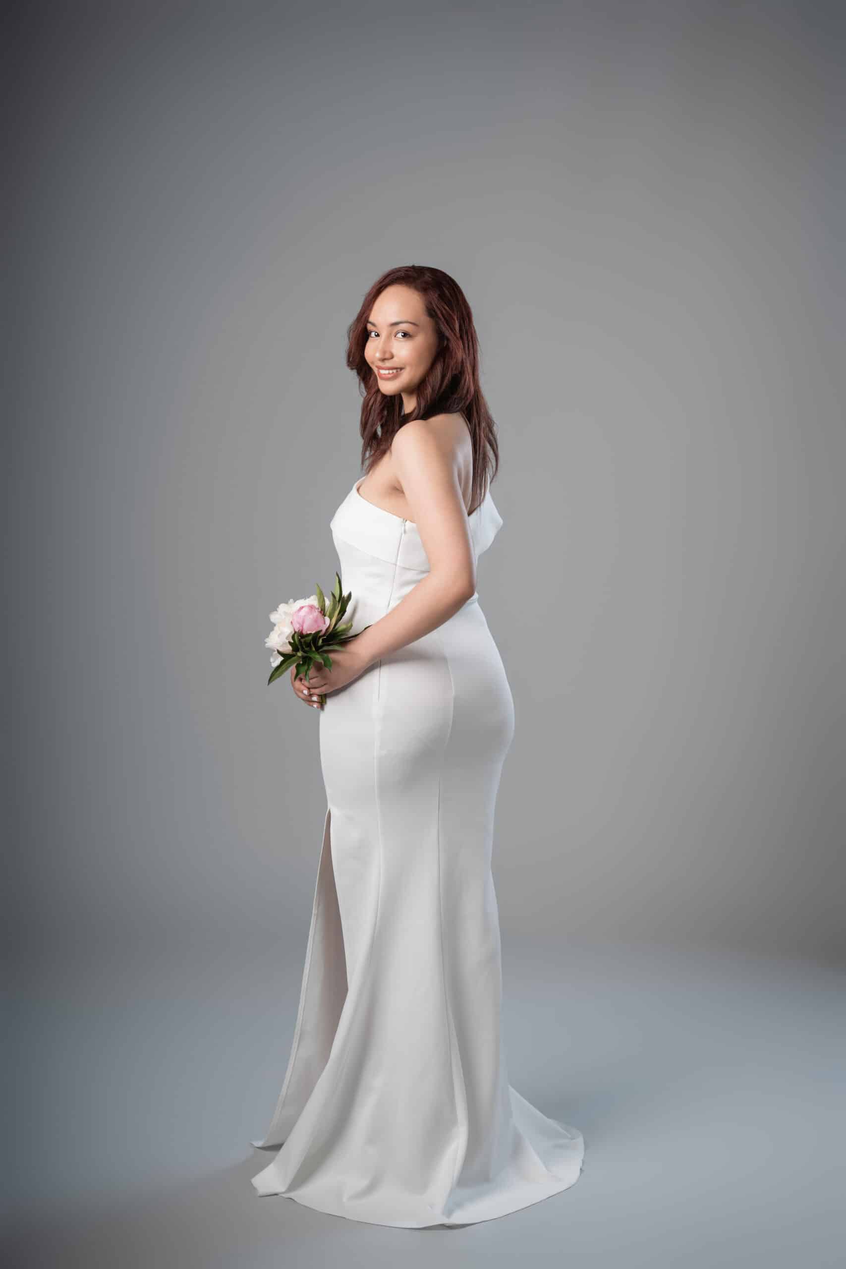 Side view of fitted white mermaid dress with ruffled neckline and front slit