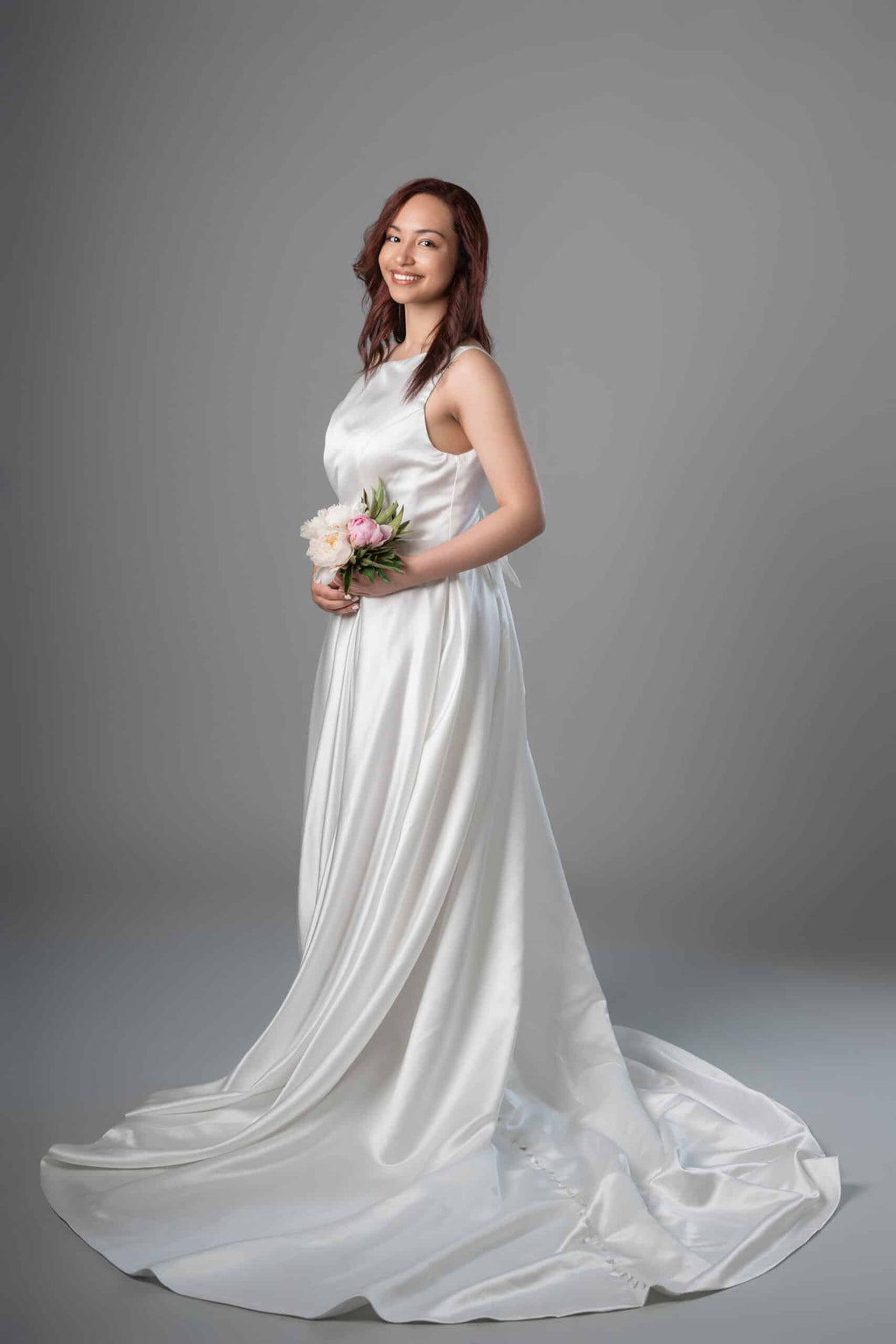 Side view of sleeveless satin A-line bridal gown showing flowing skirt and long button-trimmed train