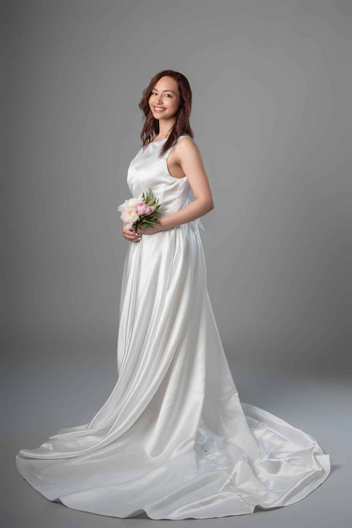 Side view of sleeveless satin A-line bridal gown showing flowing skirt and long button-trimmed train