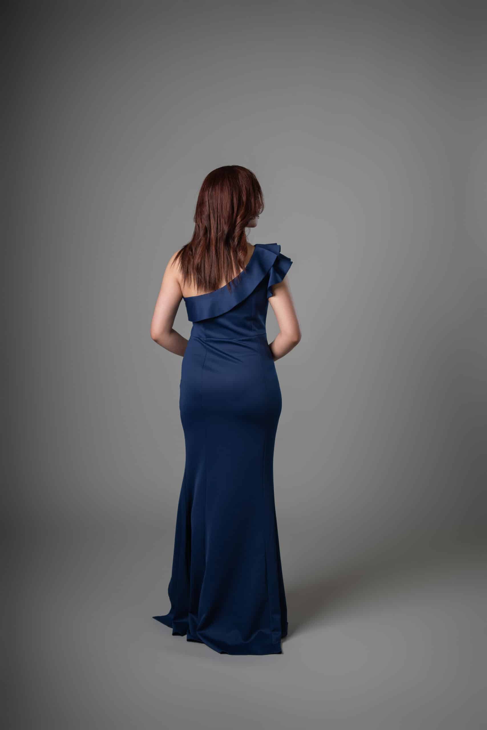 Rear view of navy mermaid gown showing elegant ruffled shoulder and flowing train detail