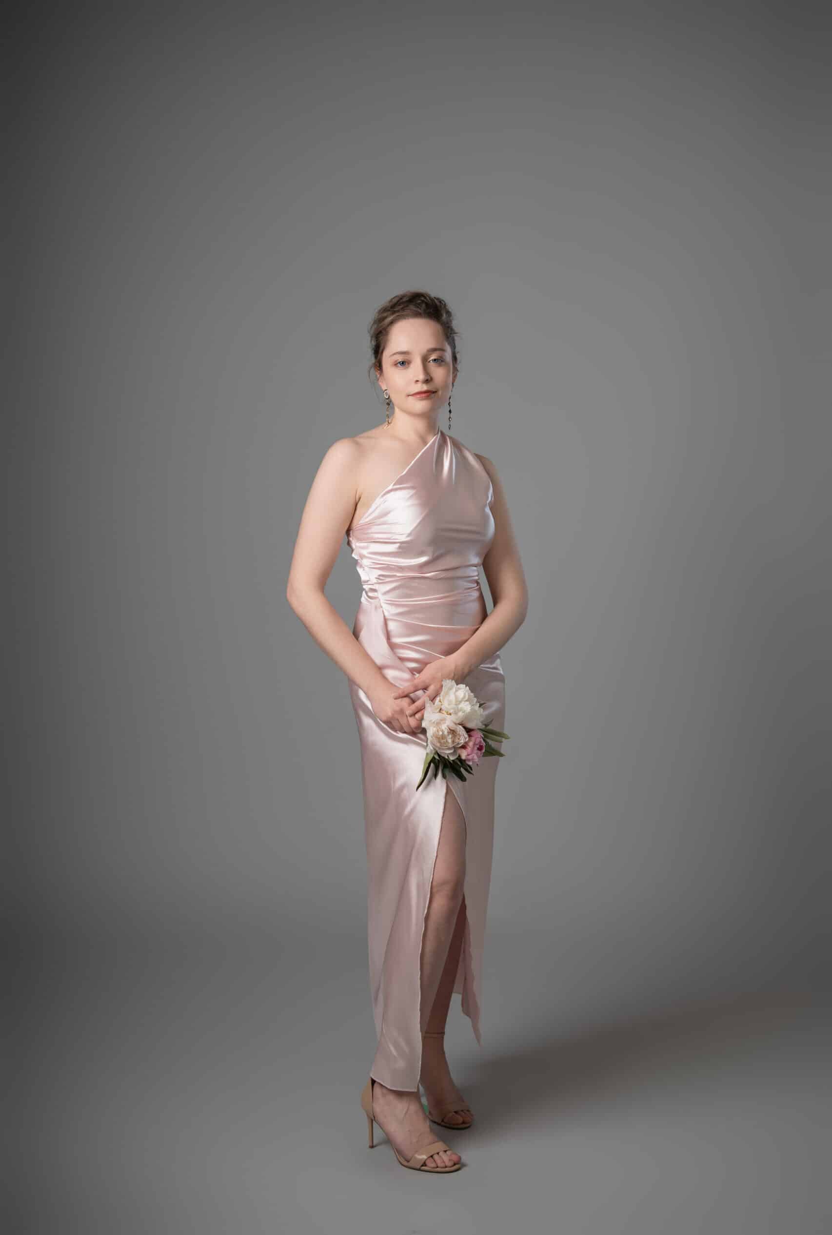 Front view of pale pink one-shoulder bridesmaids dress with fitted waist ruching and leg slit