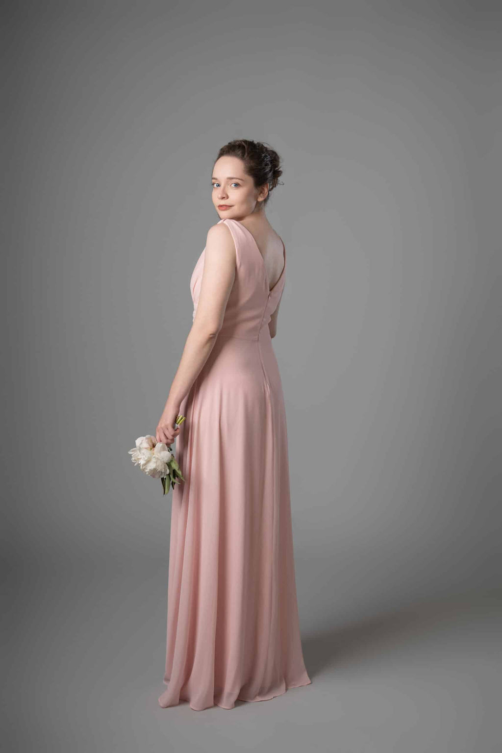Model in dusty rose V-neckline chiffon bridesmaids dress, back three-quarter view with flowing floor-length skirt