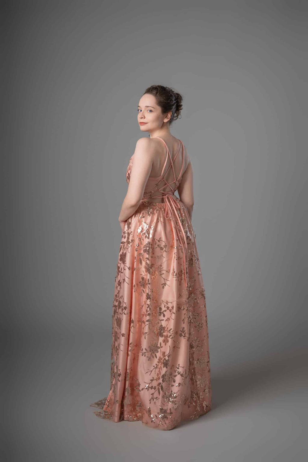 Back view showing delicate strappy cross-back detail on peach gold sequin gown