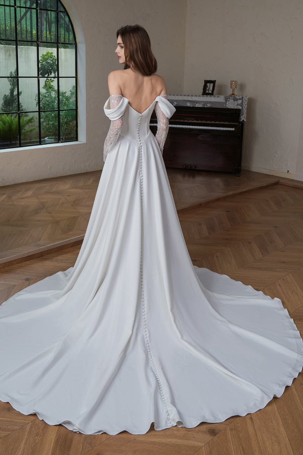 Back view of the off shoulder A-line bridal gown showing covered buttons trailing down a sweeping satin train