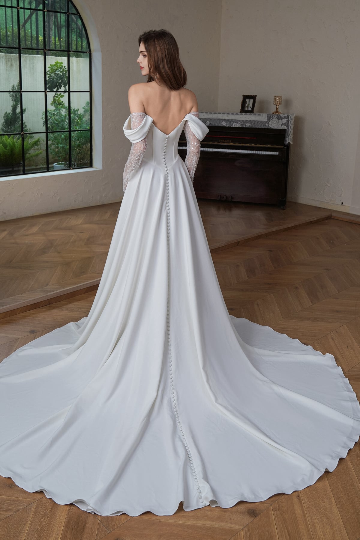 Back view of the off shoulder A-line bridal gown showing covered buttons trailing down a sweeping satin train