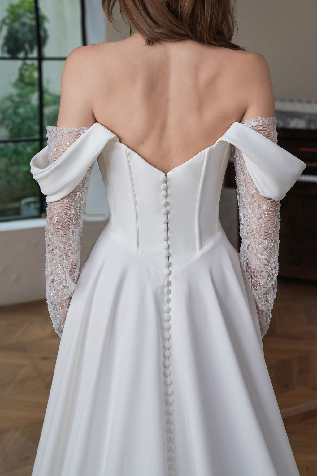 Close-up of corseted V-back with satin buttons, draped off-shoulder cuffs and beaded lace sleeves