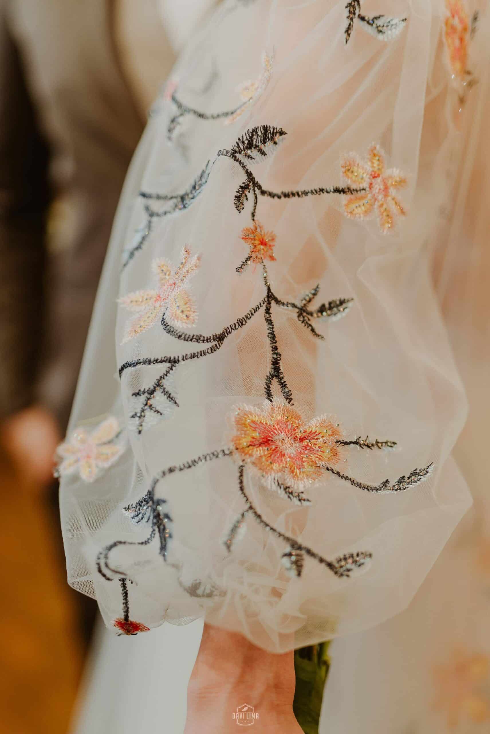Close-up of intricate beaded floral embroidery detail on tulle wedding dress fabric with botanical motifs