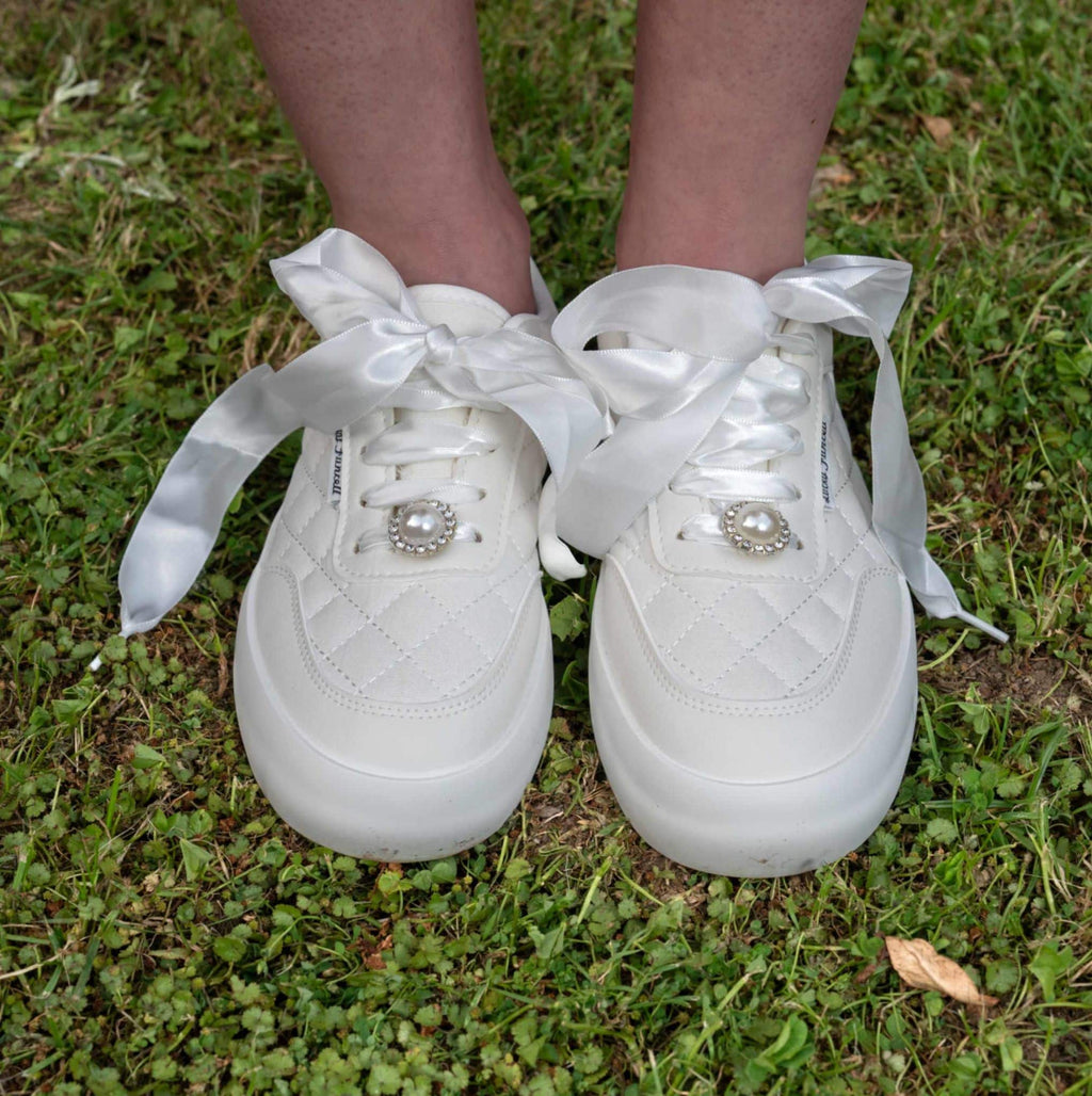 Close-up of white quilted bridal sneakers with satin ribbon laces and pearl embellishments