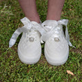 Close-up of white quilted bridal sneakers with satin ribbon laces and pearl embellishments