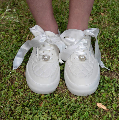 Close-up of white quilted bridal sneakers with satin ribbon laces and pearl embellishments